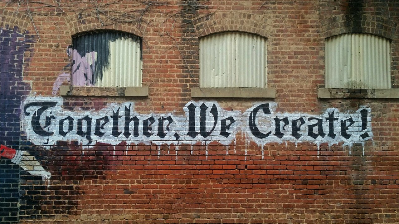 Together We Create Graffiti art on a brick wall saying "Together We Create!"